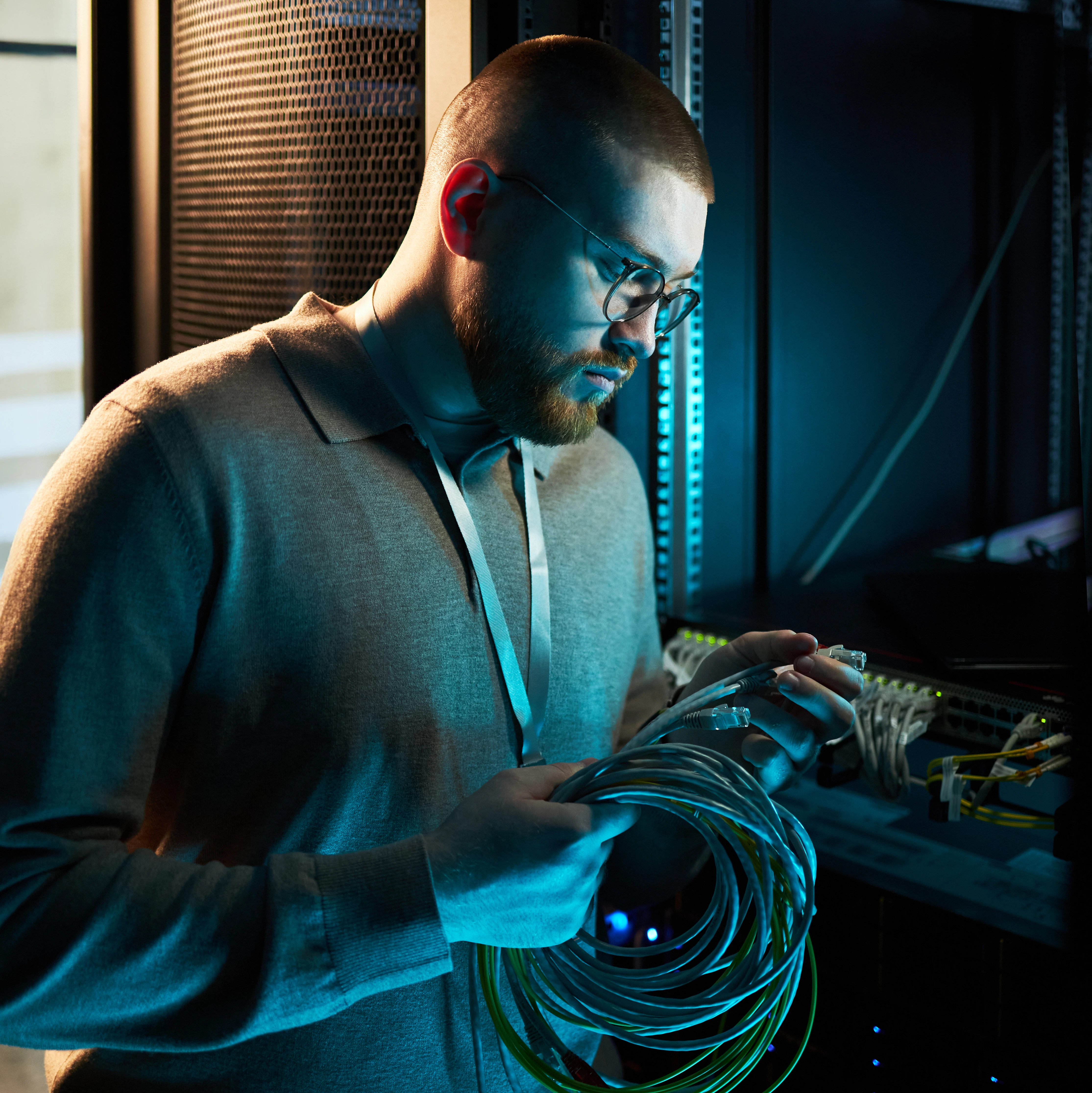 A technician in the data center holds a network cable and looks thoughtfully at the server racks.